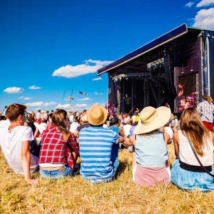 5 people sitting on grass looking at a festival stage