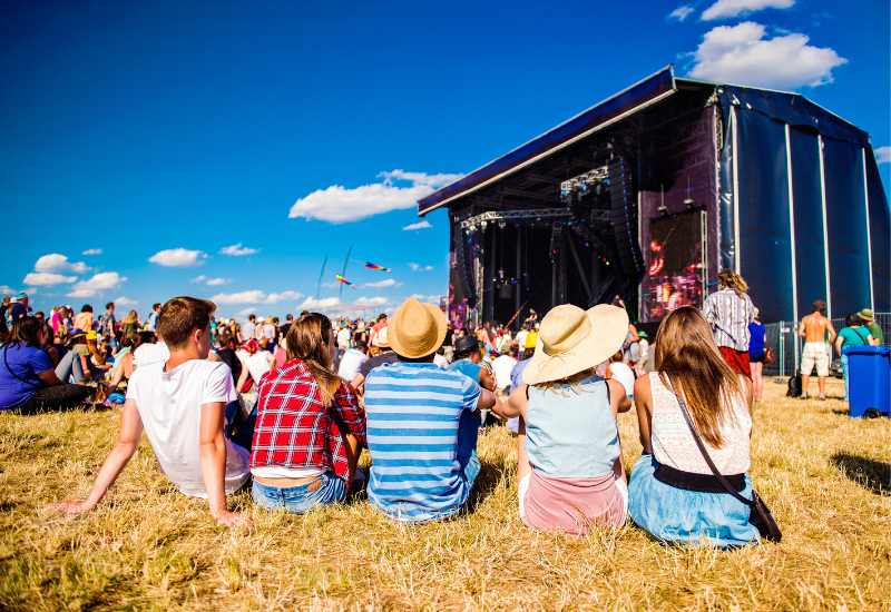 5 people sitting on grass looking at a festival stage